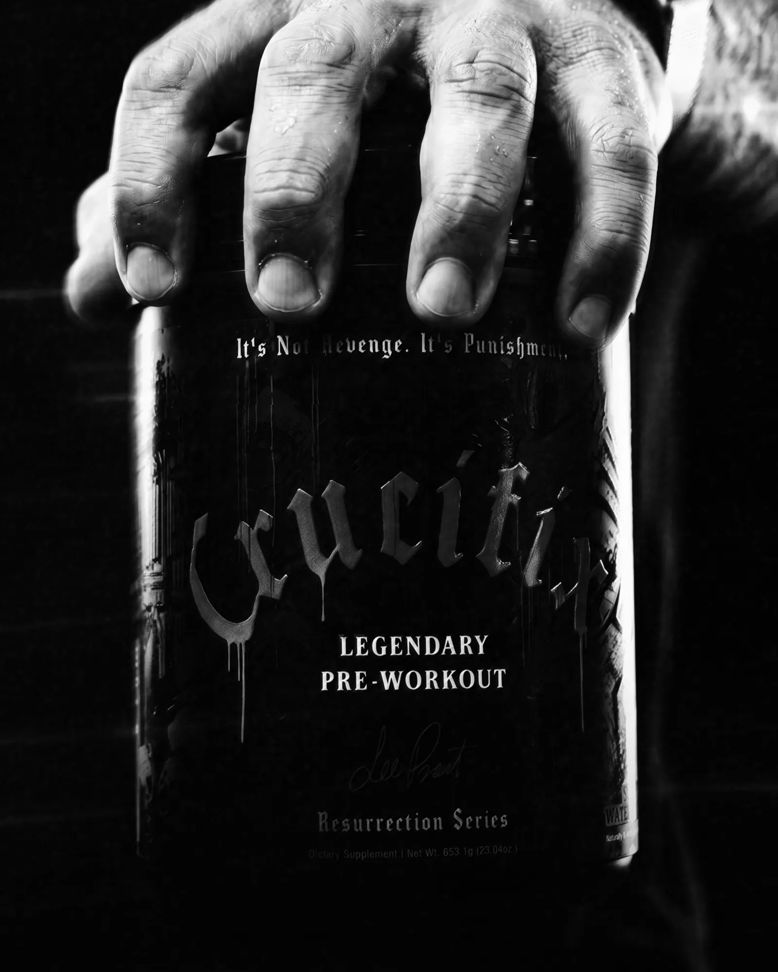 Black-and-white close-up of a hand on a NutriFitt Crucifix Legendary Pre-Workout tub from the Resurrection Series.