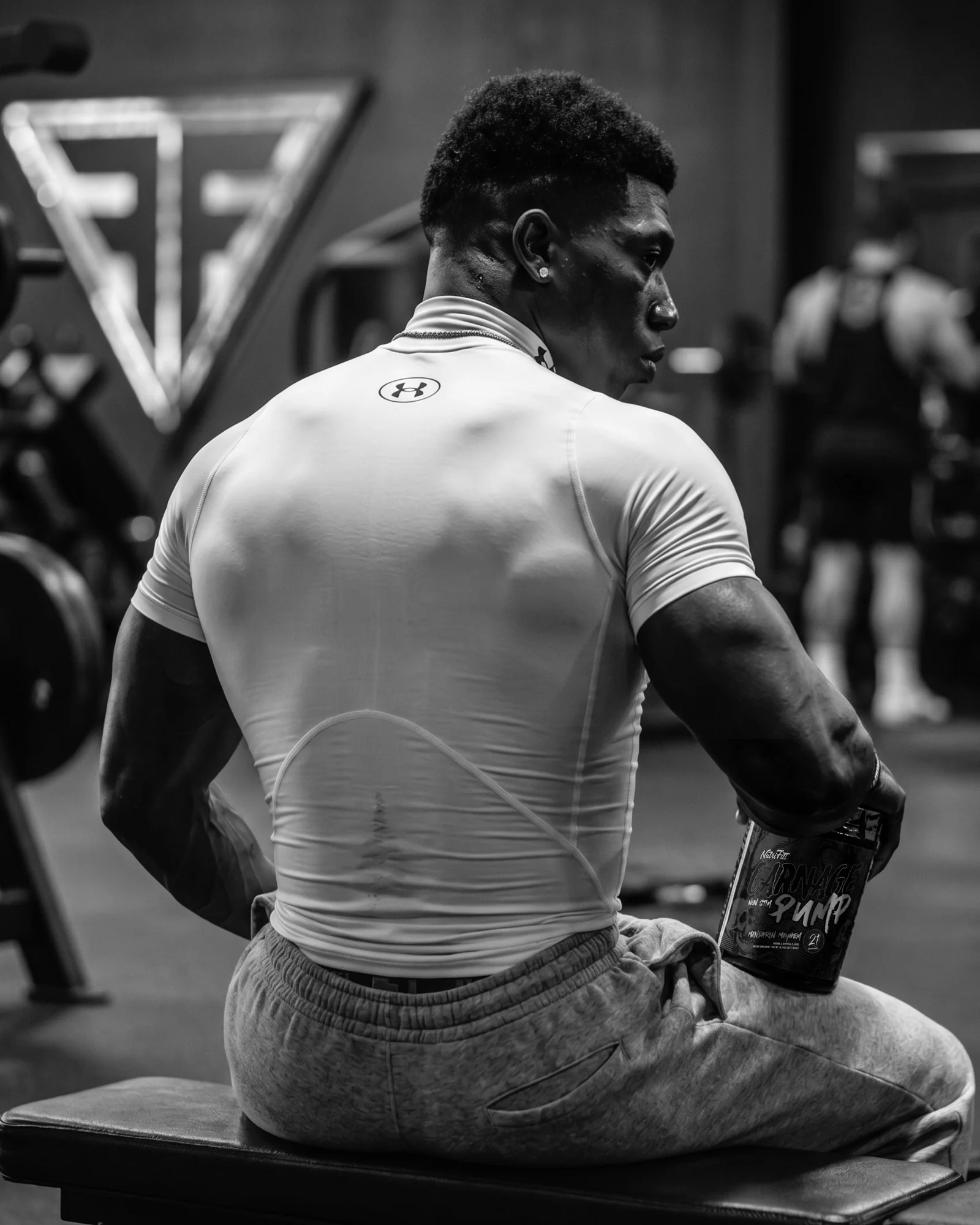 Black-and-white gym portrait of a seated athlete holding NutriFitt Carnage Pump Mandarin Mayhem.