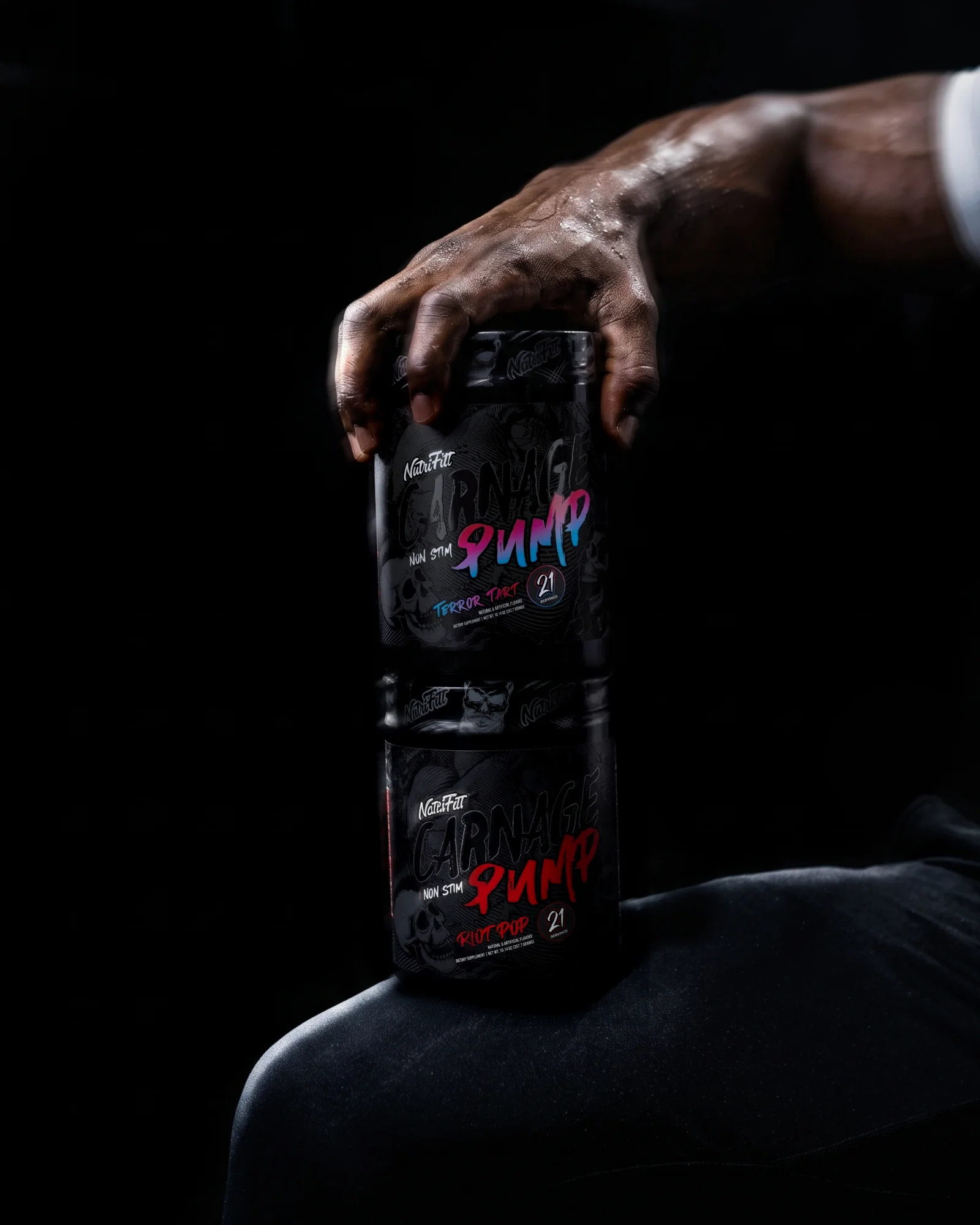 Sweaty athlete's hand resting on stacked NutriFitt Carnage Pump Terror Tart and Riot Pop tubs.