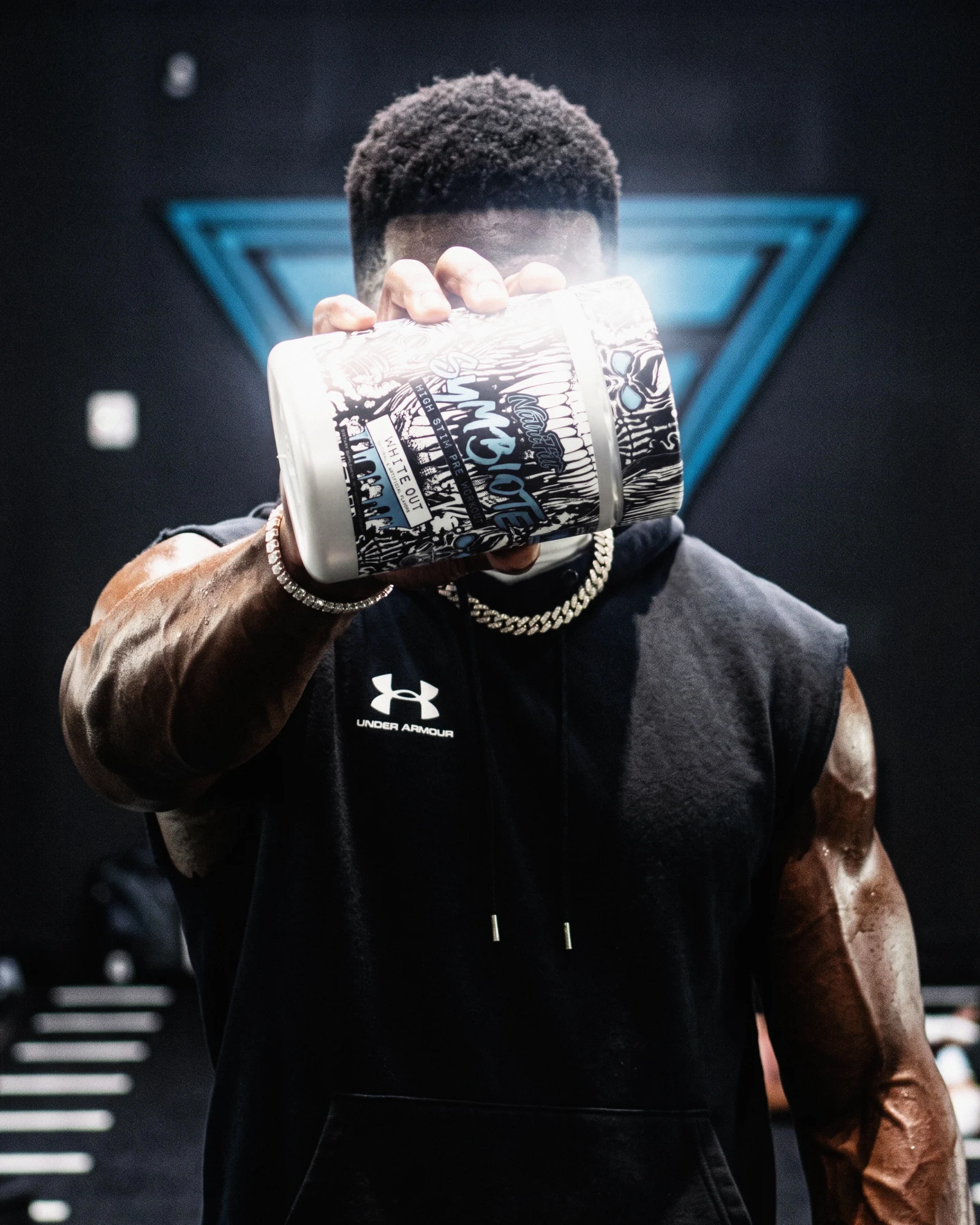 Athlete holding a NutriFitt Symbiote White Out tub toward the camera in a dark gym.