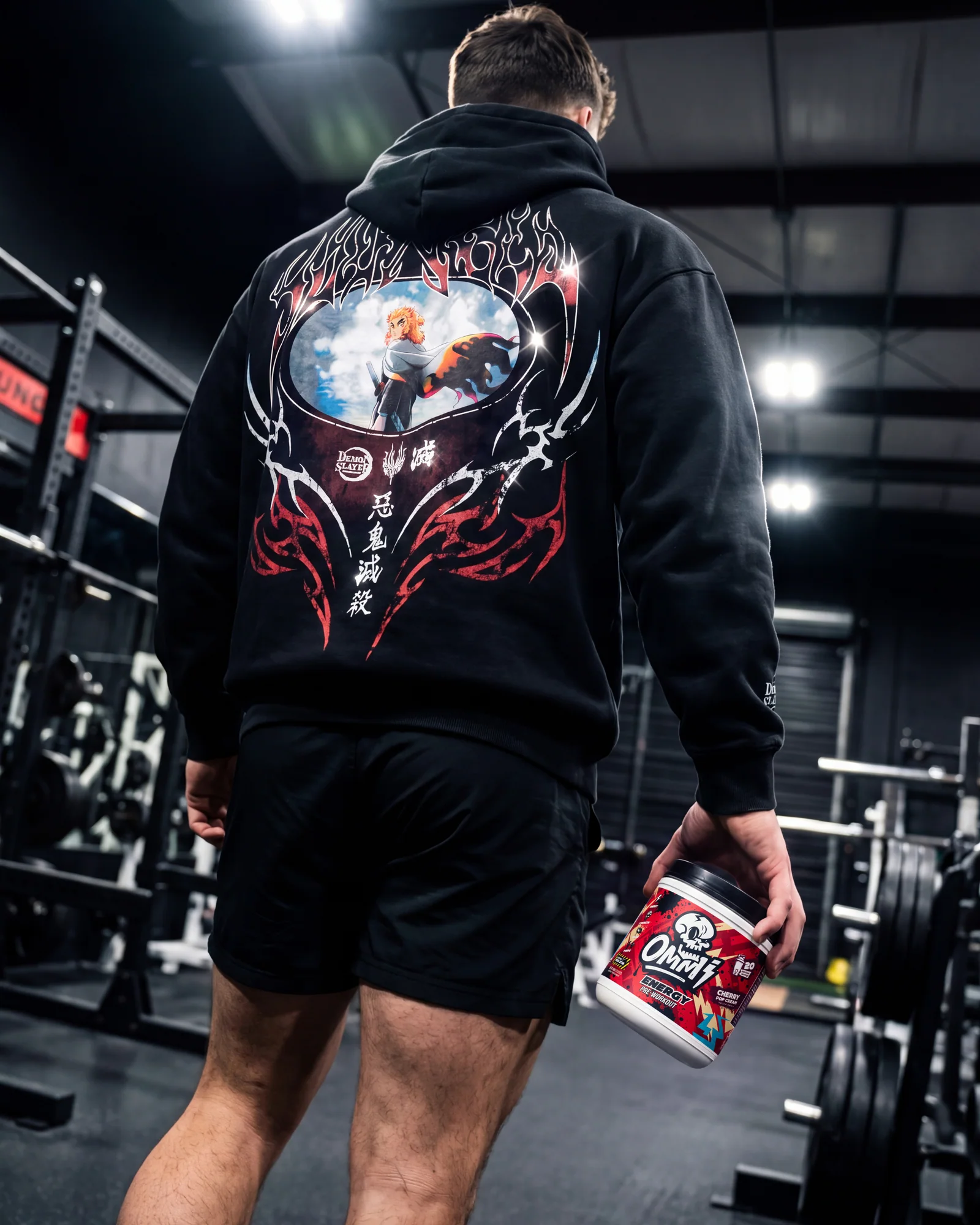 Athlete in a black graphic hoodie carrying Ommi Energy Cherry Pop Cream pre-workout through a dark gym.
