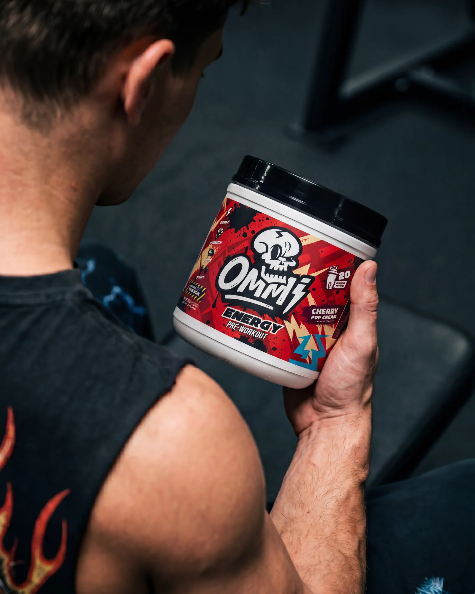 Athlete examining an Ommi Energy Cherry Pop Cream pre-workout tub in a dark gym.