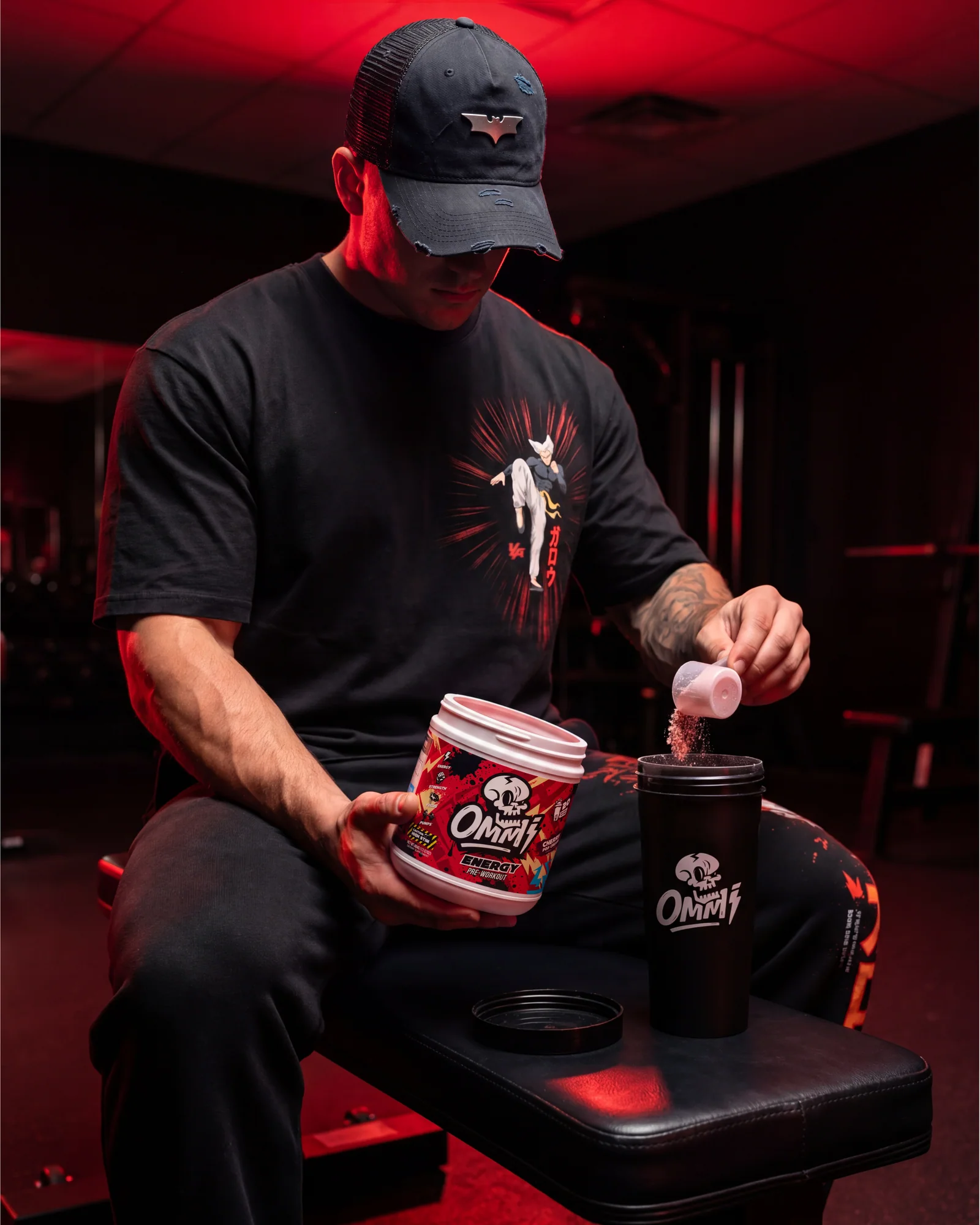 Athlete in a red-lit gym pouring Ommi Energy Cherry Pop Cream pre-workout into a black shaker.