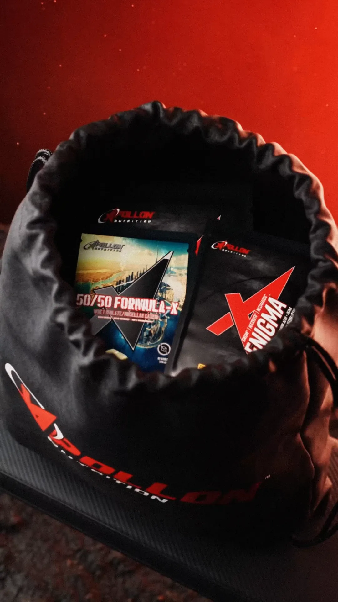 The black Apollon drawstring bag sits open with 50/50 Formula-X and Enigma sample sachets inside.