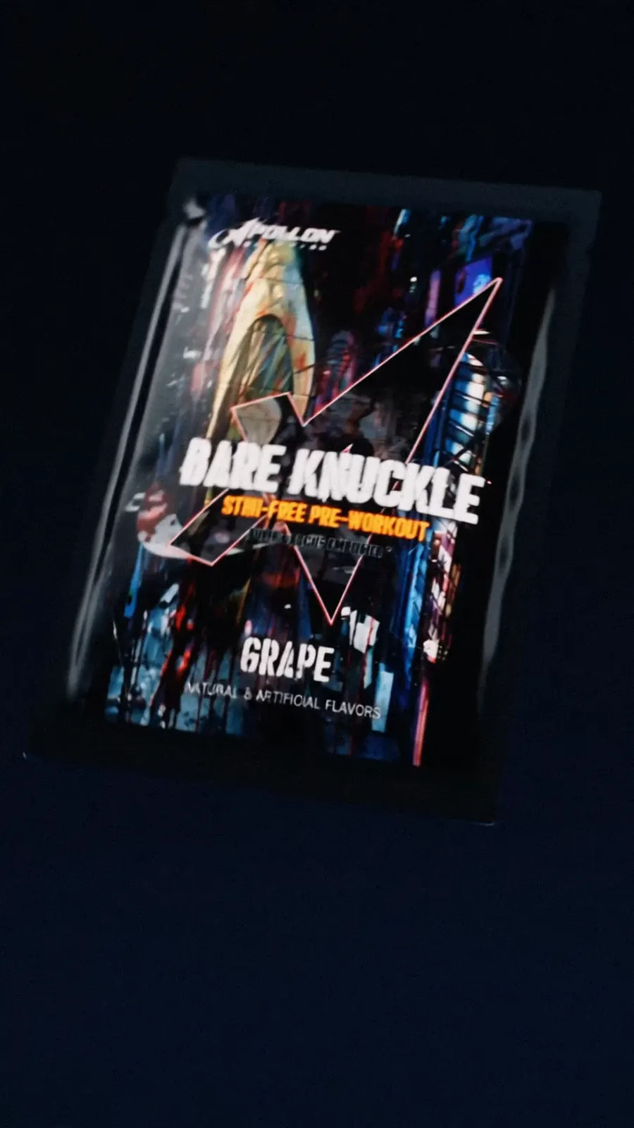 A Bare Knuckle stim-free pre-workout sachet in grape floats in blue-black light.