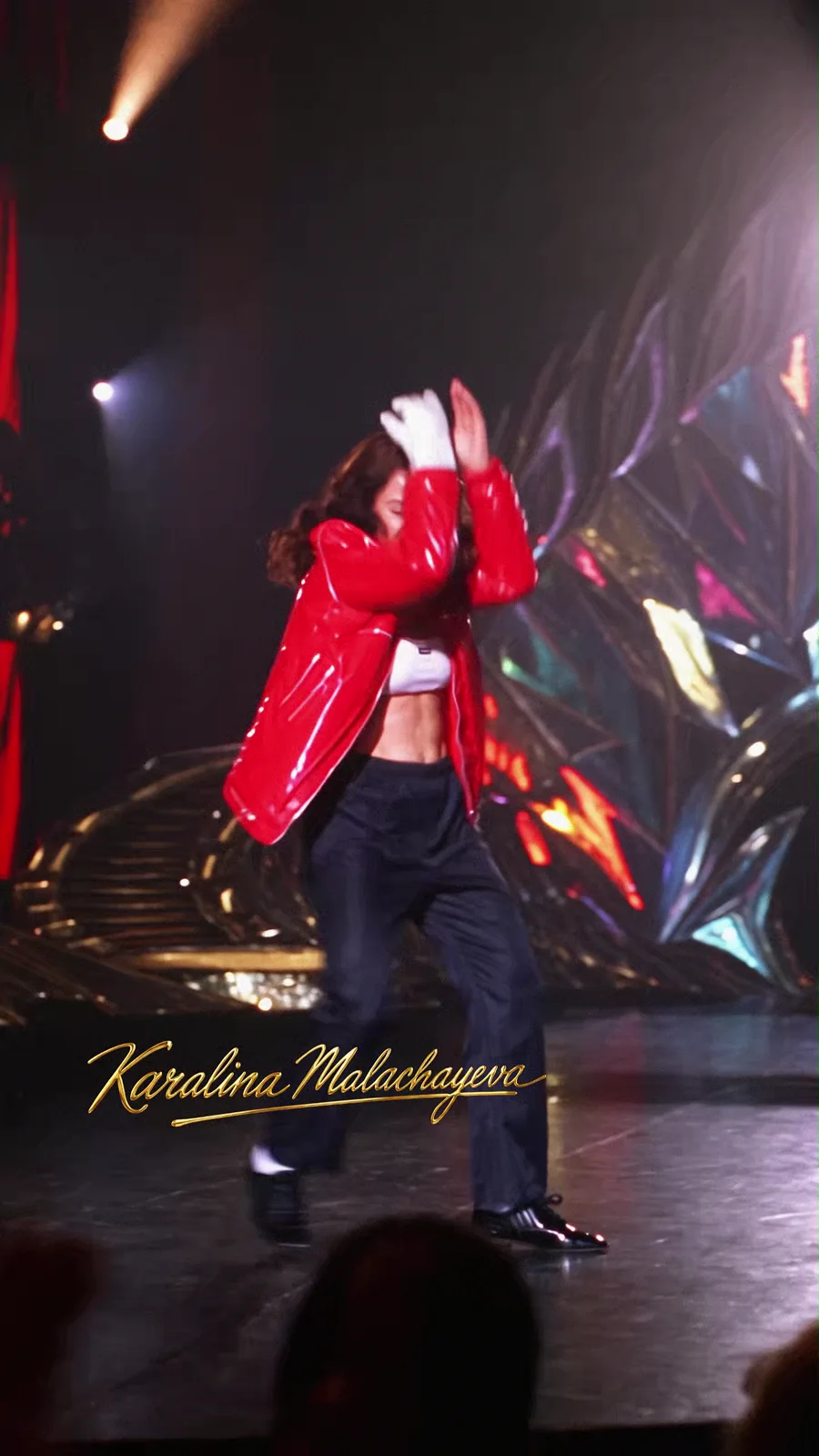 A performer in a red jacket beneath dramatic stage lighting.