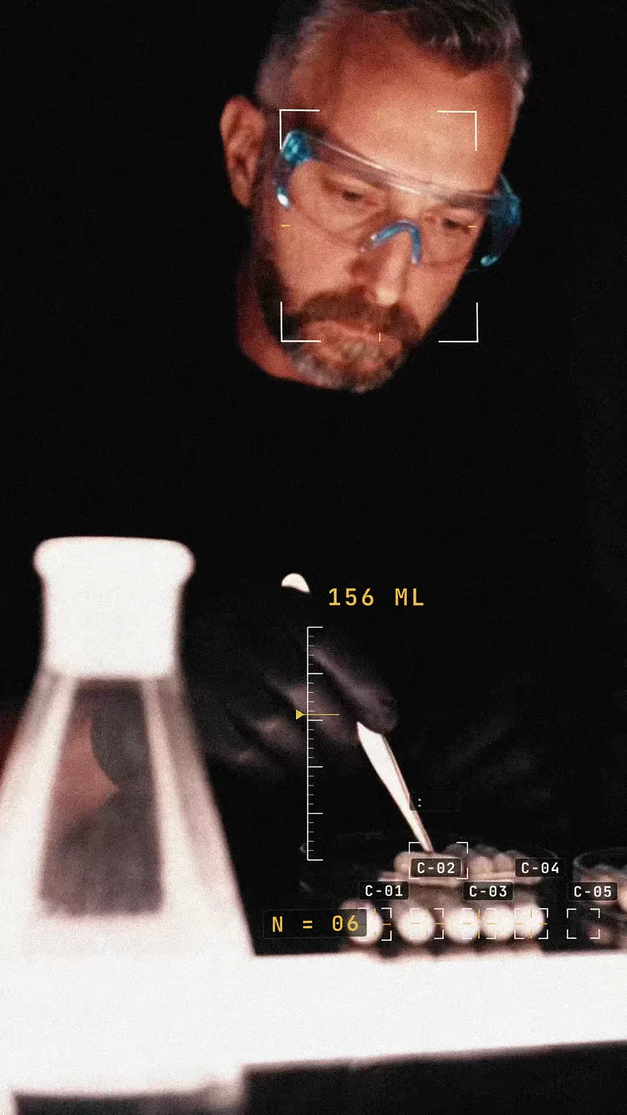 Scientist in safety glasses measuring white capsules beside a glass flask with a lab readout overlay.
