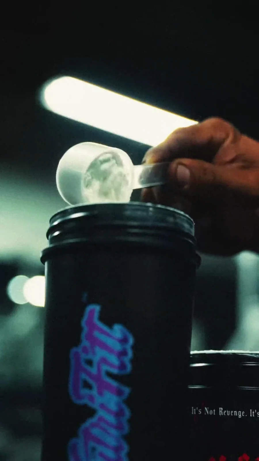 Lee Priest holds a scoop of pre-workout above a black branded shaker beside the Crucifix tub.