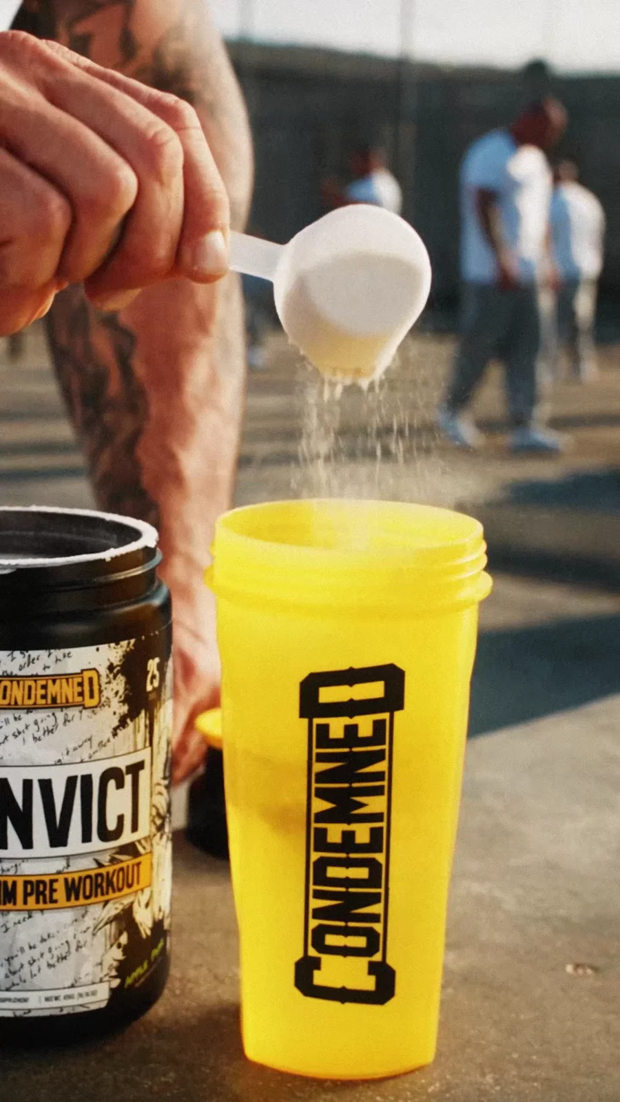 A scoop of powder pours into a yellow Condemned shaker beside a Convict tub.