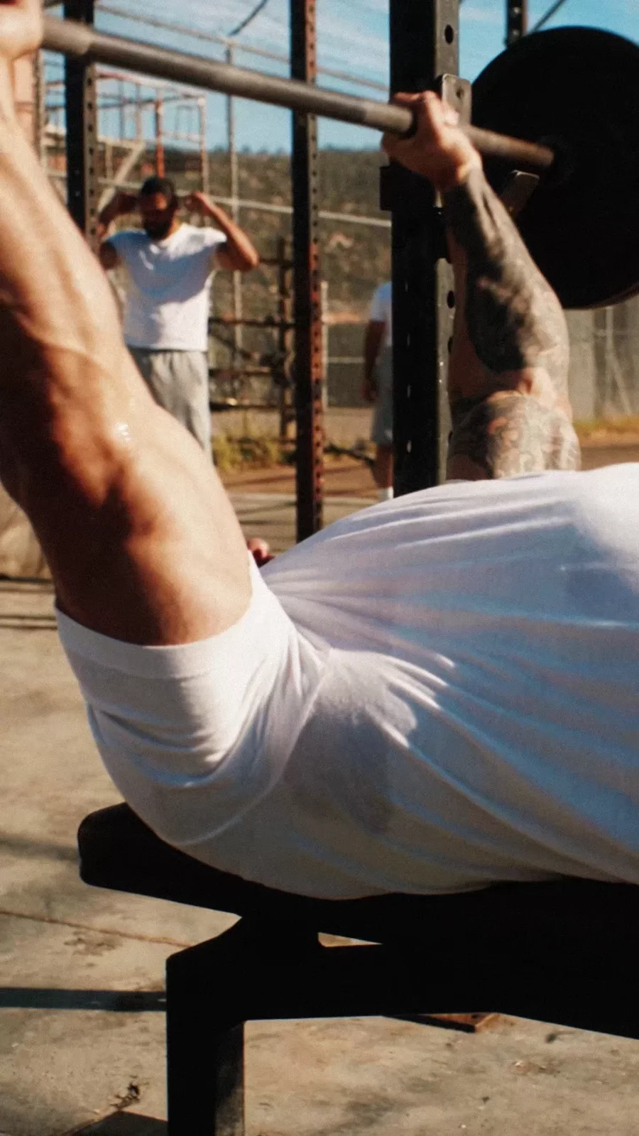 An athlete presses a barbell on an outdoor bench in the training yard.