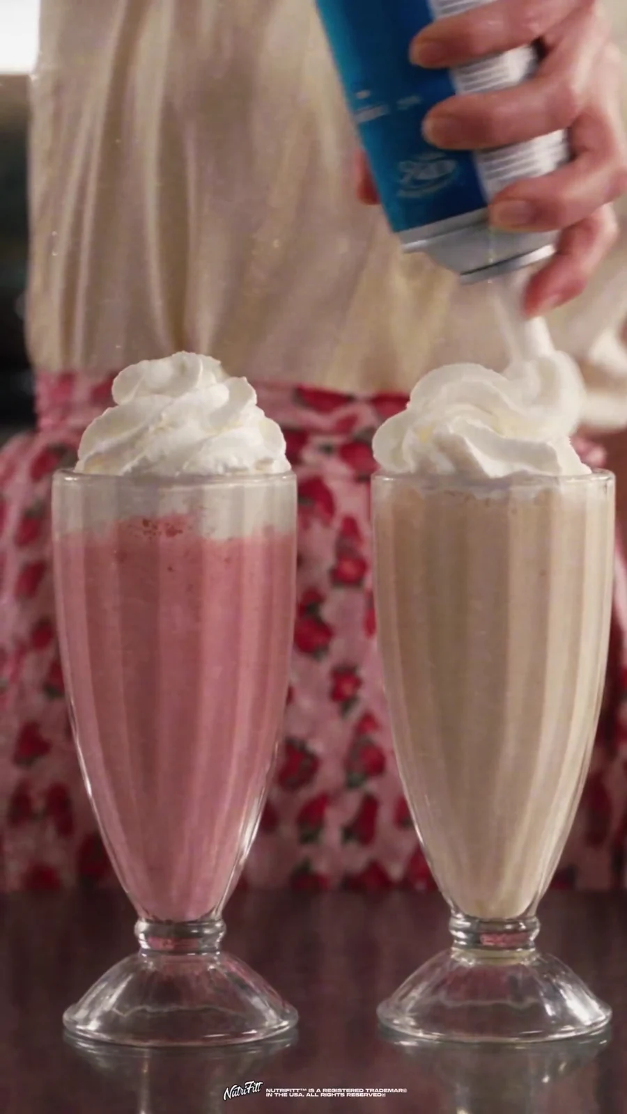 Whipped cream is sprayed onto finished pink and vanilla collagen milkshakes.
