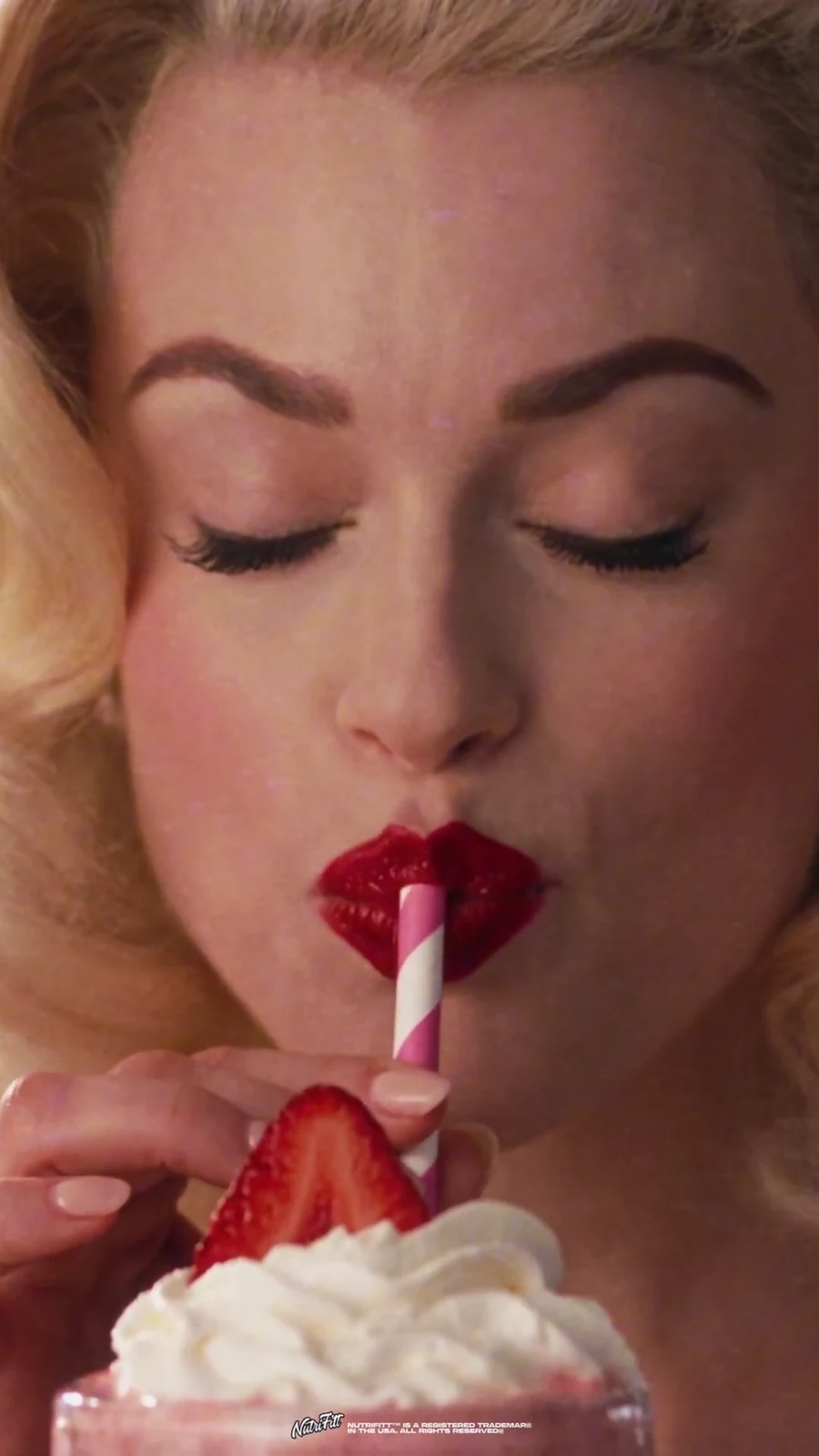 Diner guest tastes a strawberry-topped collagen milkshake through a striped straw.