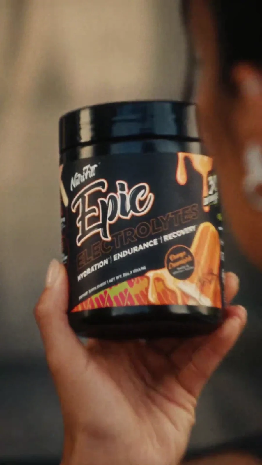 Hand holds a black Epic Electrolytes mango tub in a tight product close-up.