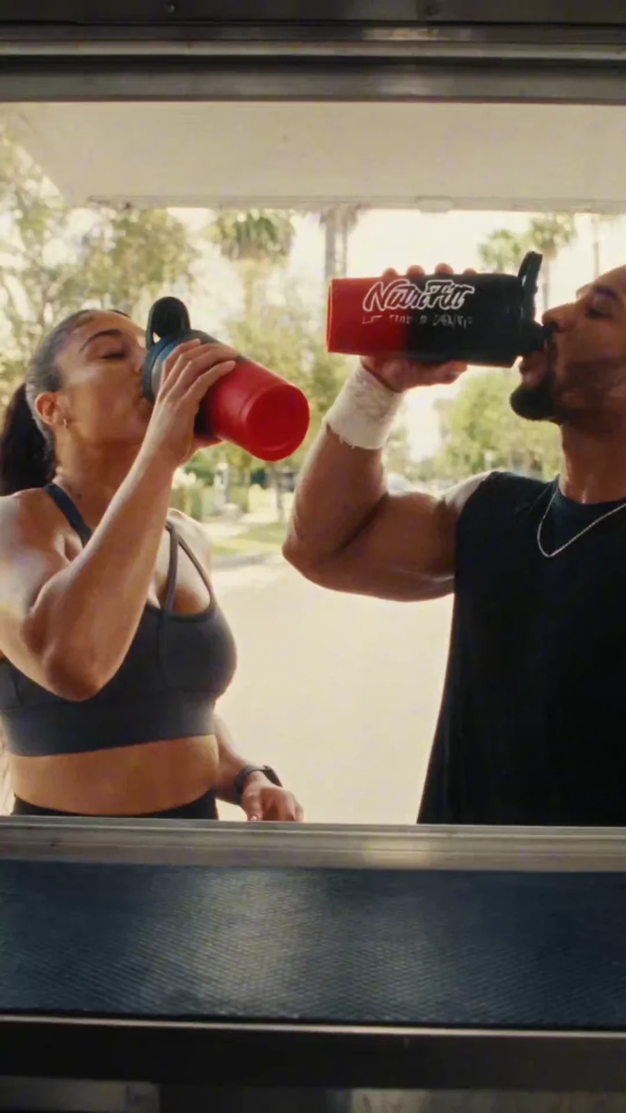 Two athletes drink from red and black NutriFitt shakers beside the Epic hydration lineup.