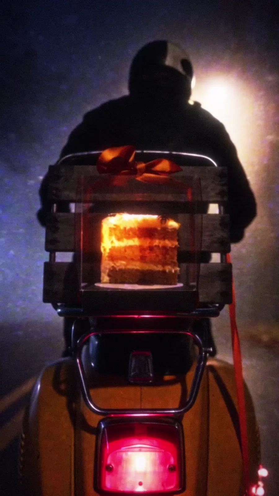 Rear view of the scooter in fog, a glowing slice of pumpkin spice cake strapped in a ribboned crate above the red tail light.