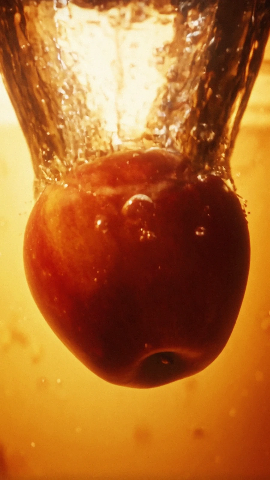 Glossy red apple suspended as golden cider crashes around it.