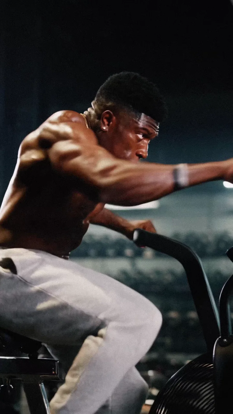 An athlete drives through an air-bike sprint in a dark training space.
