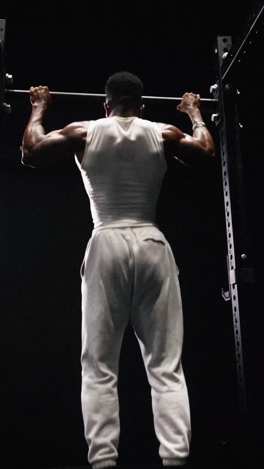 An athlete performs a pull-up beneath the gym lights.