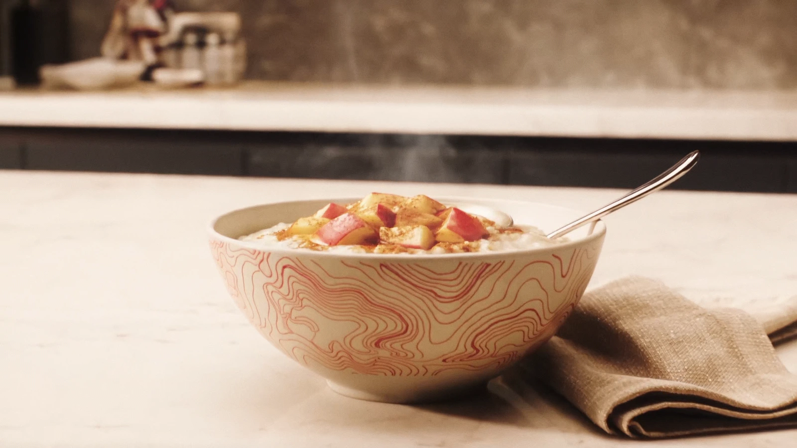 Warm apple-cinnamon creamy rice bowl with spoon on a bright stone kitchen counter.