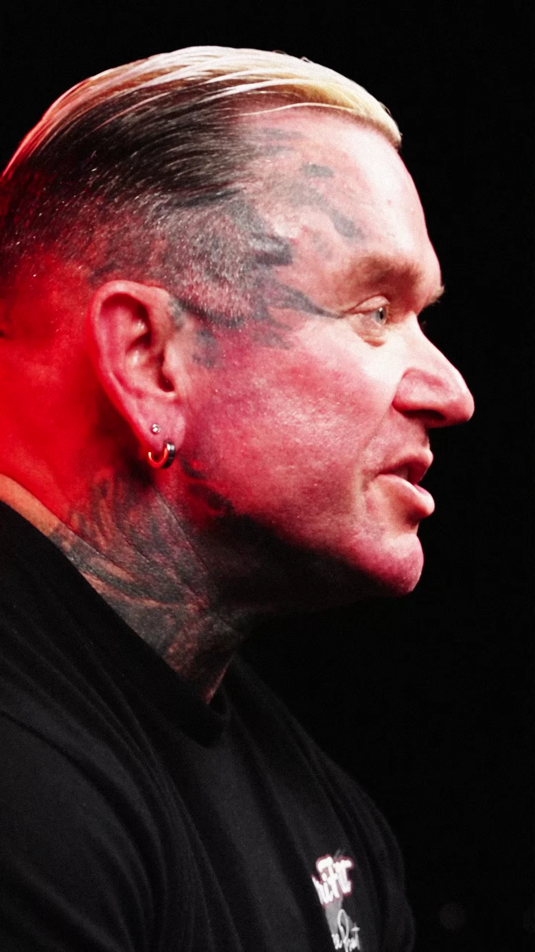 Close-up side profile of Lee Priest speaking, with red edge lighting against a black background.