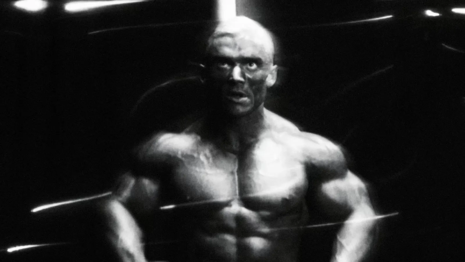 Black-and-white portrait of Lee Priest, shirtless, staring into camera through streaks of light.
