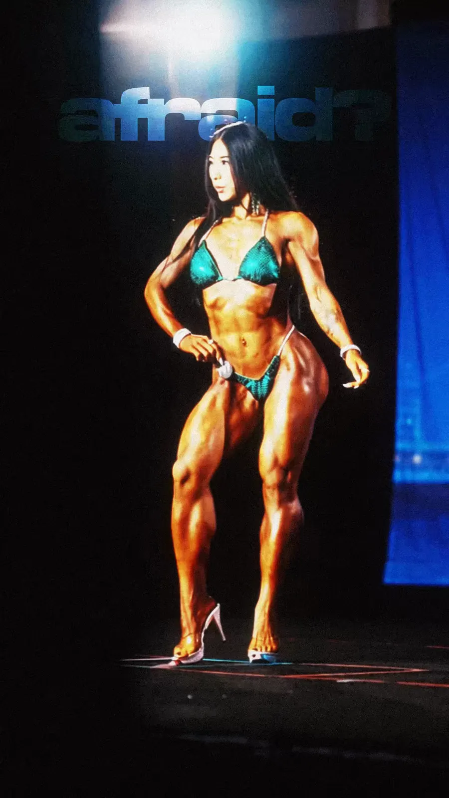 A bikini competitor holds a front pose on stage.