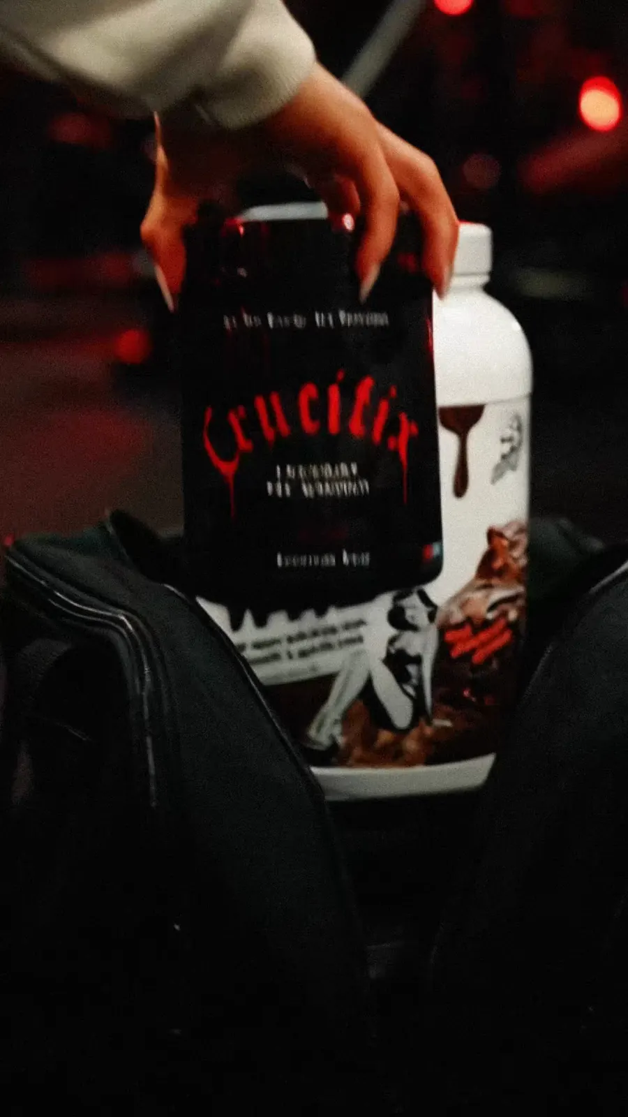 A hand lifts a Crucifix pre-workout tub out of a gym bag.