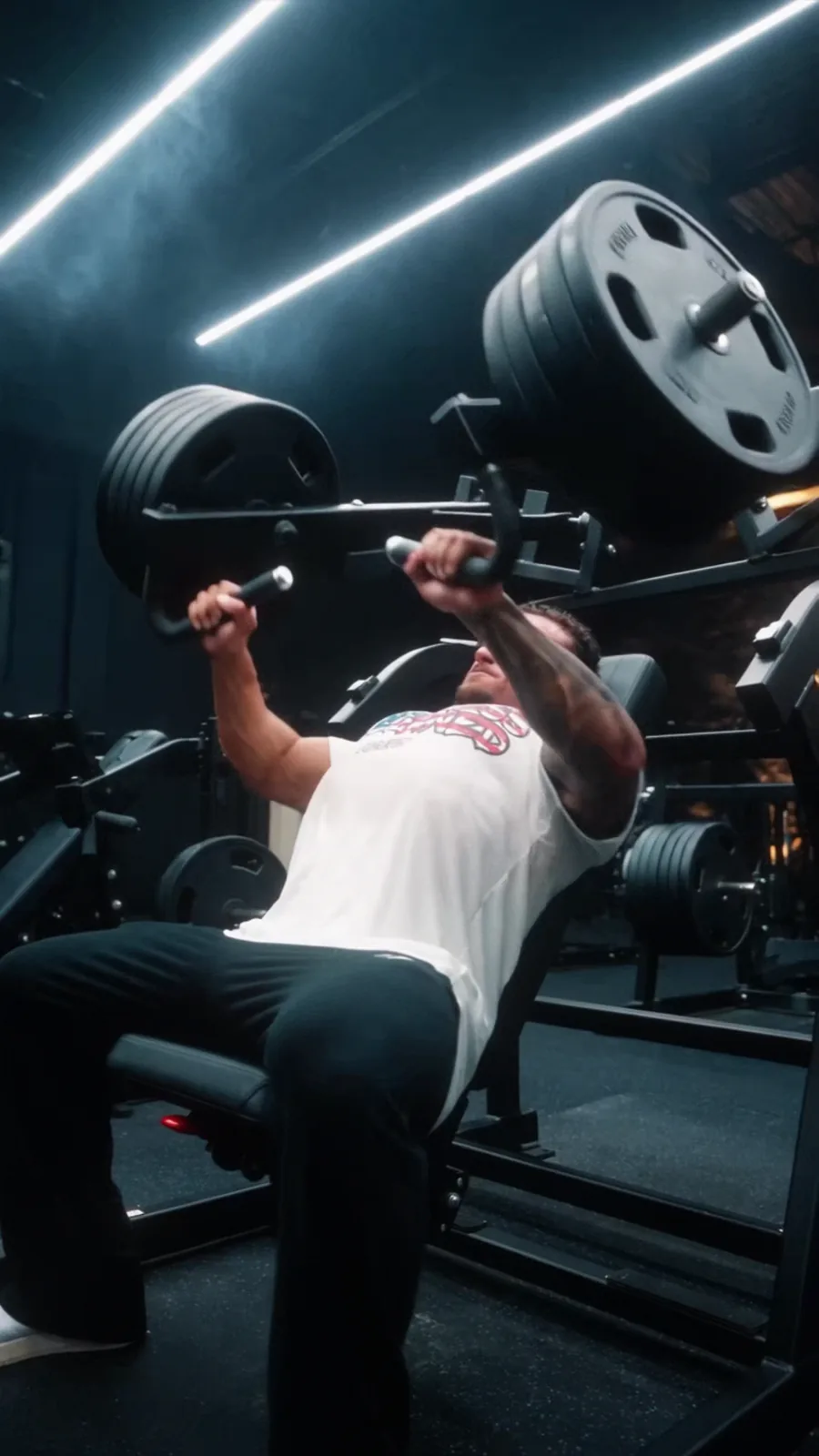 Cesare drives a plate-loaded chest press beneath the geometric lights of a dark gym.