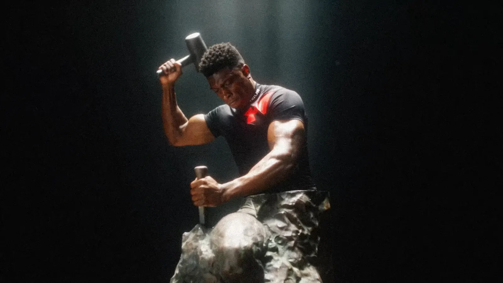 TheOneCay swings a sledgehammer onto a boulder in a dark studio.