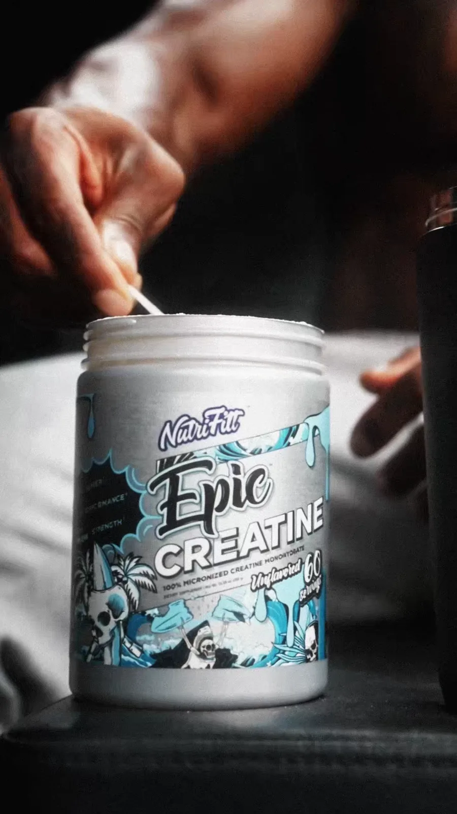 A hand measures a serving from a silver NutriFitt Epic Creatine tub.