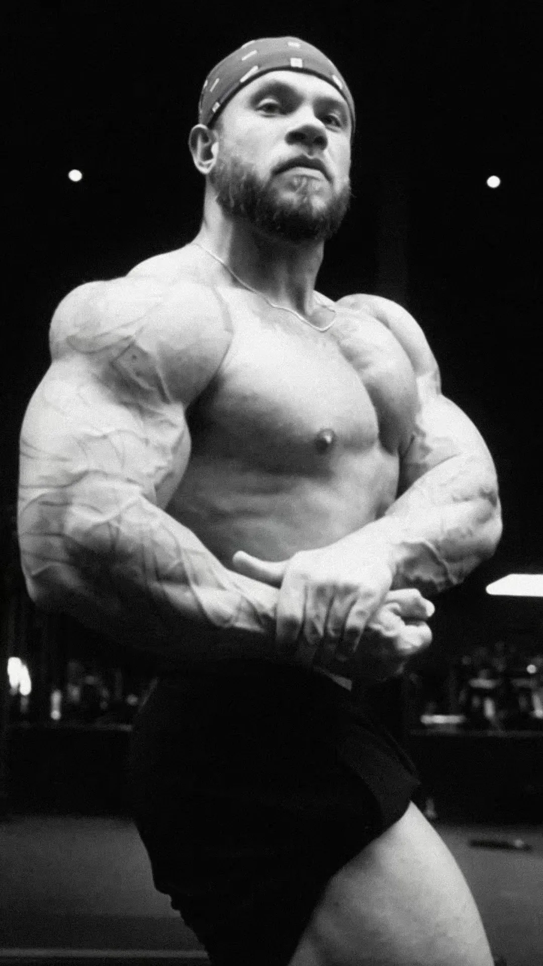 A bodybuilder in a bandana hits a most-muscular pose in black and white.