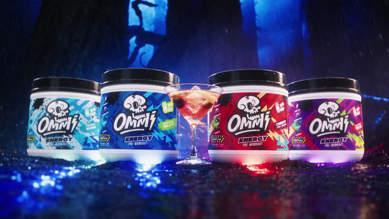 Four colorful Ommi Energy tubs arranged around a cocktail on a rain-slick forest set.