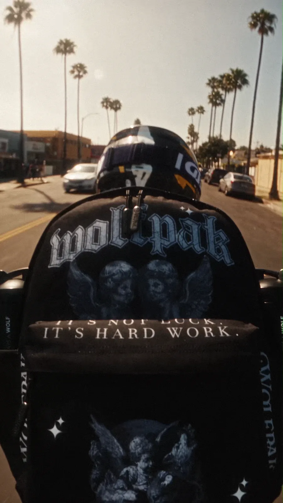 Rear-mounted view dominated by a black gothic WOLFpak backpack as the rider moves through traffic.