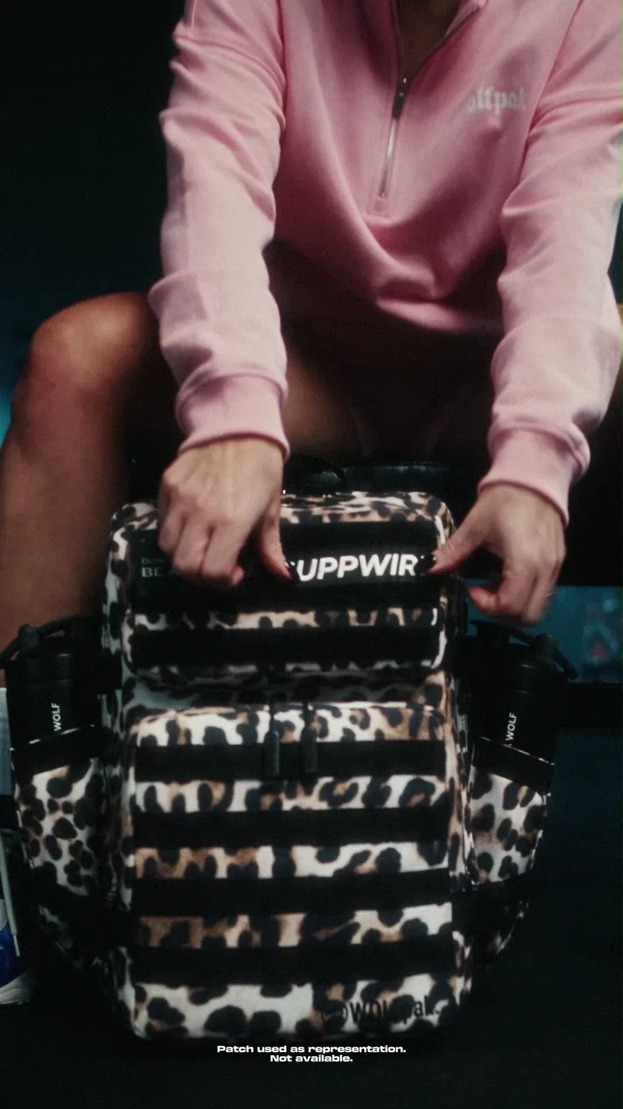 Woman in pink training wear aligns a representational Suppwire patch on a leopard-print WOLFpak bag.