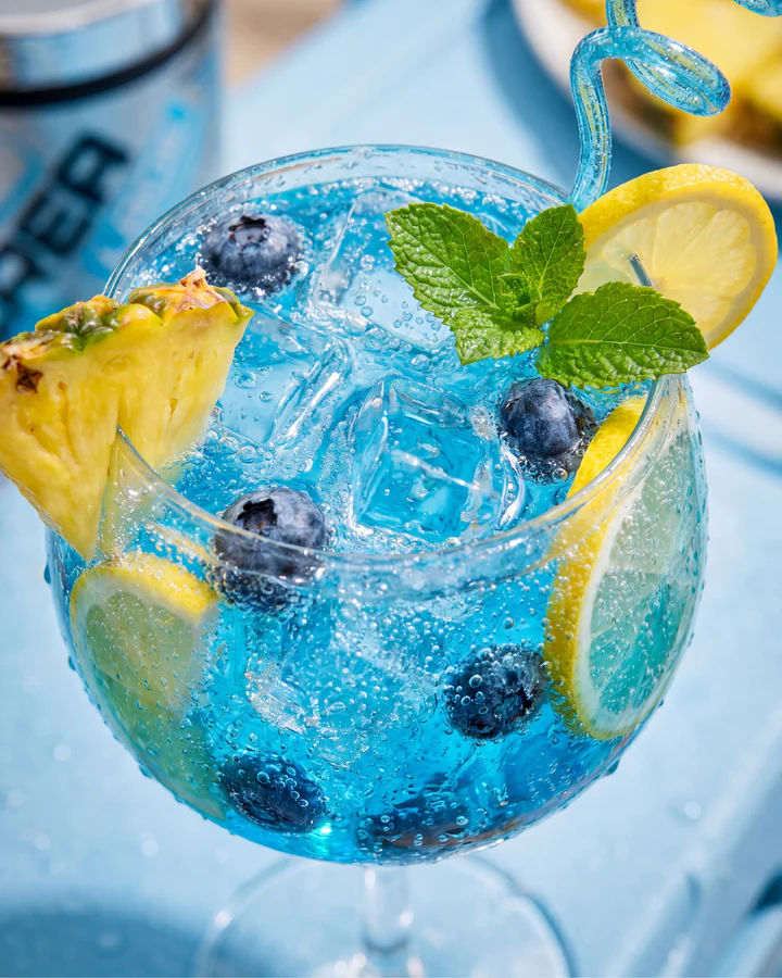 Blue iced drink with blueberries, lemon, pineapple and mint sits beside a partial CREA LADE tub.