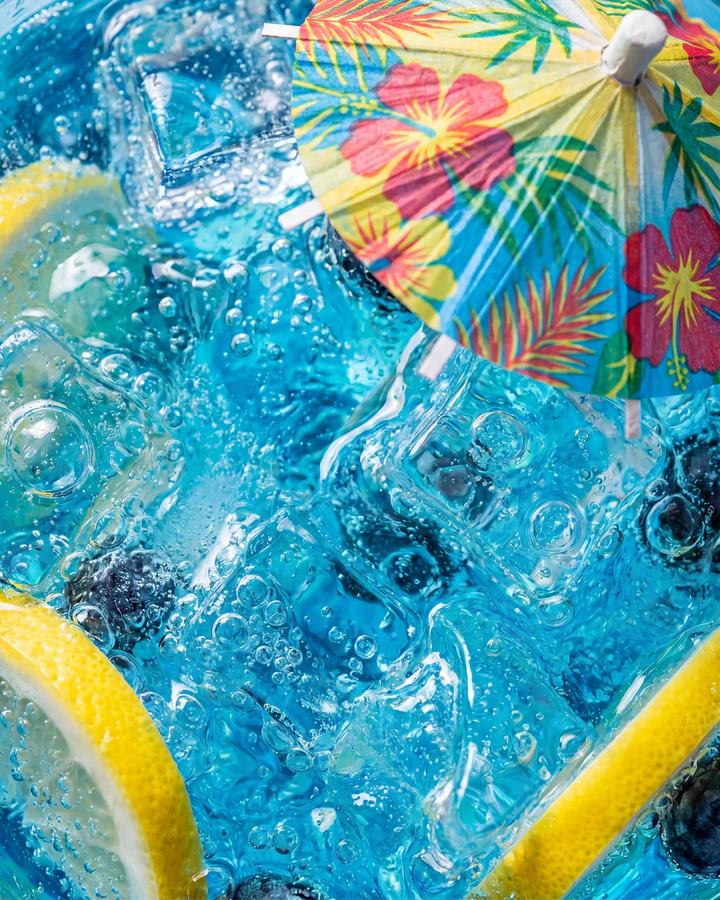 Extreme macro of a blue iced drink with blueberries, lemon and a colorful cocktail umbrella.