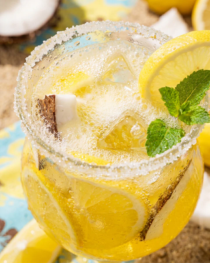 Yellow tropical iced drink with lemon, mint and coconut is viewed from above on a bright summer set.