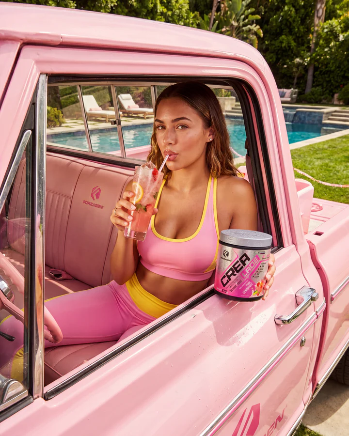 Woman leans from a pink vintage vehicle window with a pink drink and CREA LADE tub inside.
