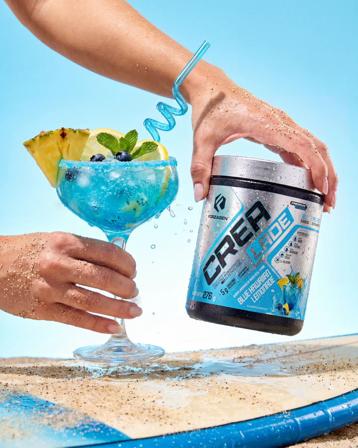 Two hands reach toward a blue CREA LADE tub and a fruit-filled blue drink on a beach table.
