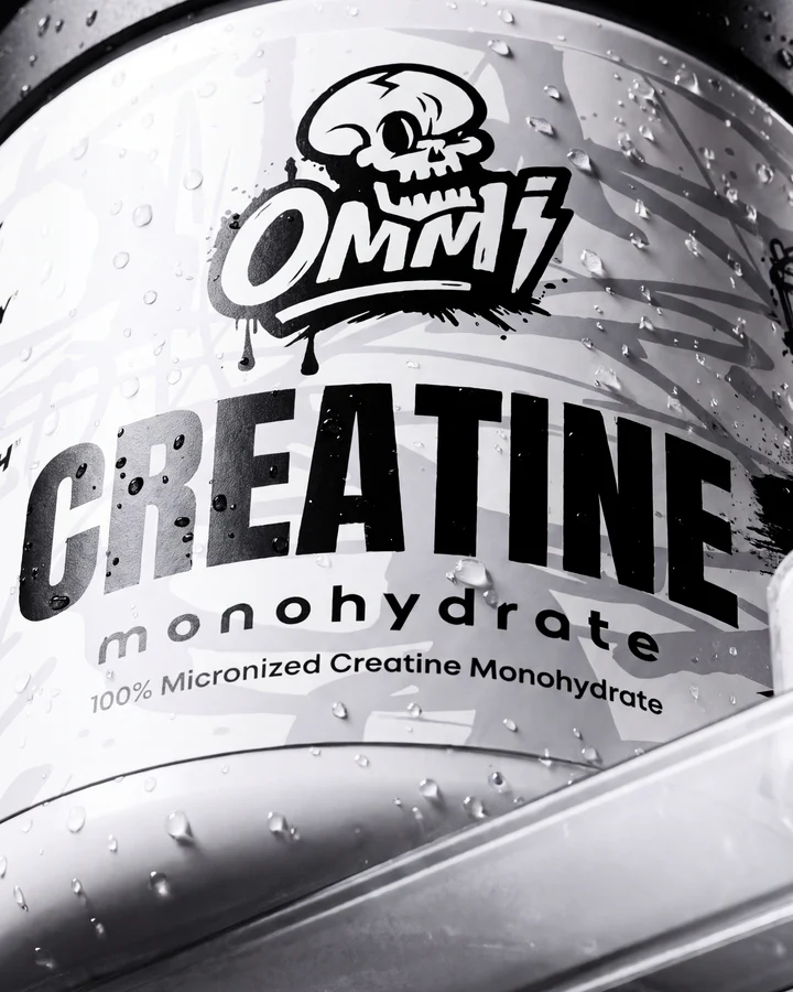 Angled close-up of the white Ommi Creatine tub rests against a reflective studio surface.