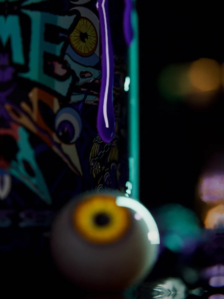 Macro of a purple drip hanging from the Dark Labs FLAME tub above a yellow-eyed eyeball on the wet stone floor, warm lights blurred behind.
