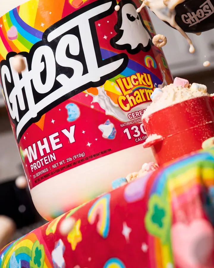 Close product view of Ghost Lucky Charms whey with a red scoop and colorful cereal set.