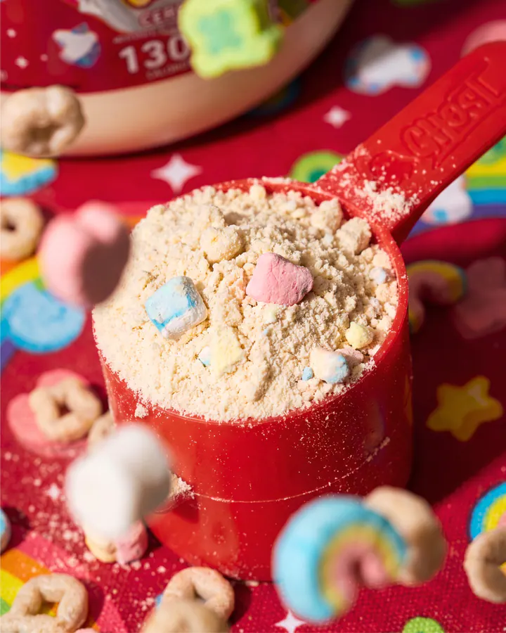 Macro view of a red protein scoop filled with Lucky Charms whey and marshmallow cereal pieces.