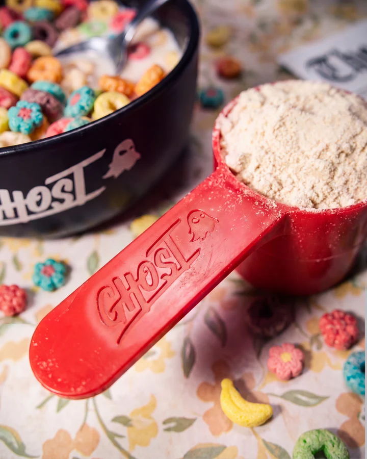 Red Ghost scoop filled with whey powder rests among colorful cereal beside a black Ghost bowl.