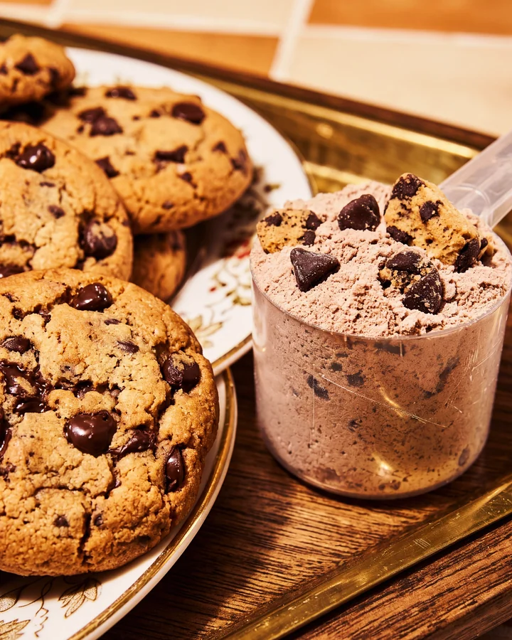 ISOCLUSIONS Chocolate chip cookies beside a scoop of chocolate protein on a tray.