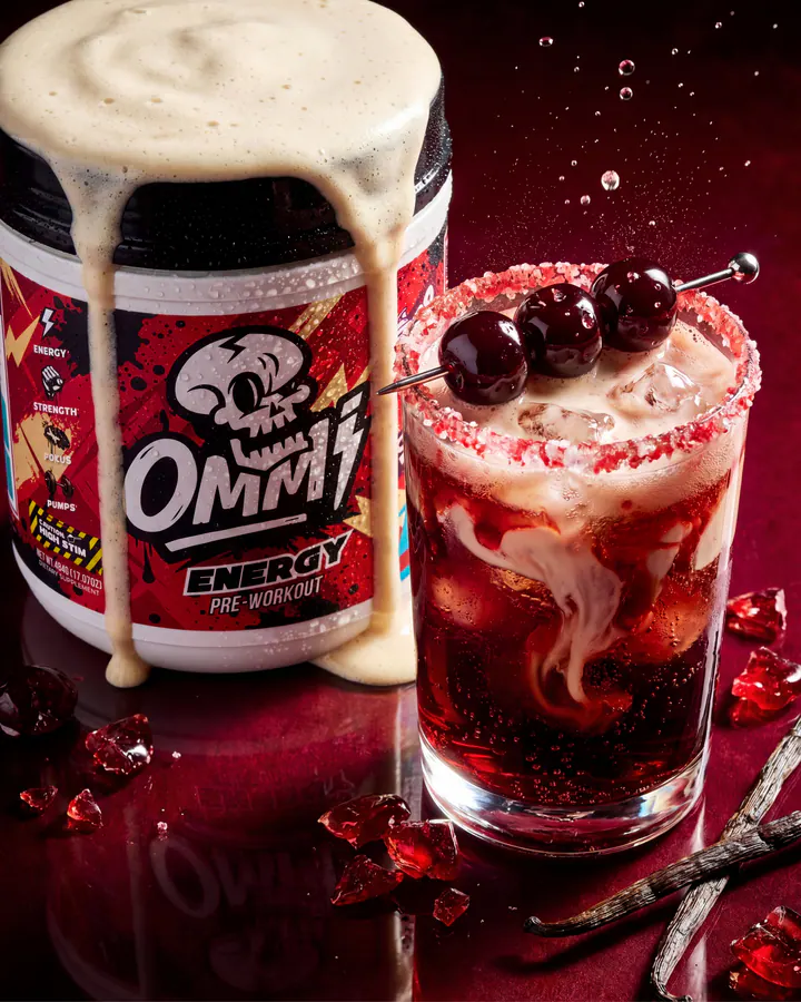 Ommi Energy tub and Cherry Pop Cream drink staged together with cherries on a reflective red surface.
