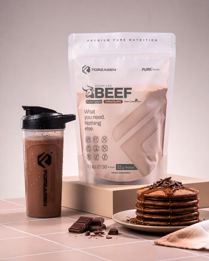 Pure Beef Chocolate protein bag and shaker beside pancakes and pieces of dark chocolate.