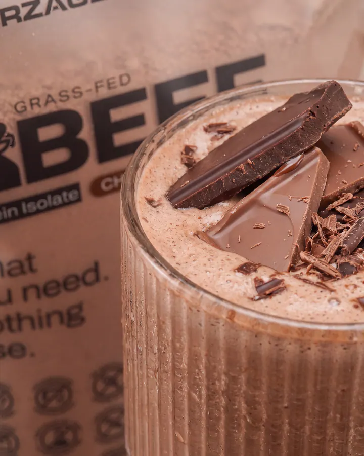 Close-up chocolate shake with chocolate pieces floating above a Pure Beef protein bag.