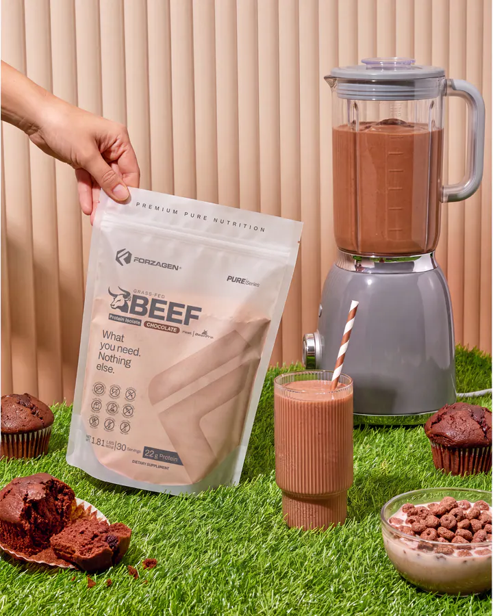 A hand adds Pure Beef Chocolate powder to a blender beside the protein bag and finished shake.