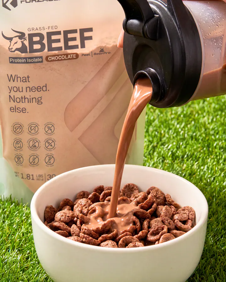 Chocolate protein drink pouring from a shaker into a cereal bowl beside Pure Beef packaging.